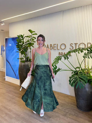 Woman in a green dress standing in an indoor setting with plants and a wall with text.